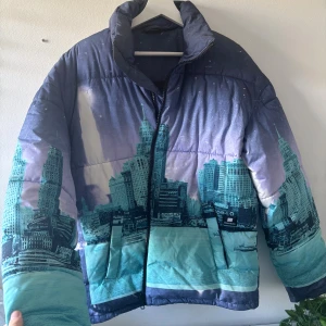 Blå pufferjacka med cityprint - Säljer en unik pufferjacka med blå och turkosa toner och ett coolt cityscape-tryck över hela jackan. Jackan har hög krage, dragkedja framtill och två fickor. Perfekt statement-piece för dig som vill sticka ut i vinterkylan. Nypris 800 kr.   Storlek XS men sitter som en M på mig och S på min bror för referens.  Tyvärr blev den aldrig min drömjacka, utan har bara testats en vinterpromenad. 🌸