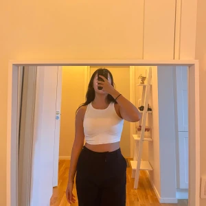 Vit croppad linnetopp - Säljer en vit croppad linnetopp med rund hals och breda axelband. Toppen är ärmlös och har en tight passform som framhäver midjan. Perfekt att styla med höga byxor eller shorts för en clean och fräsch look.