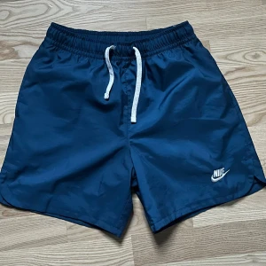 Marinblå Nike shorts med snörning - Snygga marinblå shorts från Nike med vit snörning i midjan och klassisk logga på benet. Perfekta för sommaren och träning, tillverkade i lätt syntetmaterial som torkar snabbt. Enkel och sportig design med loose passform. Köpta på Zalando 
