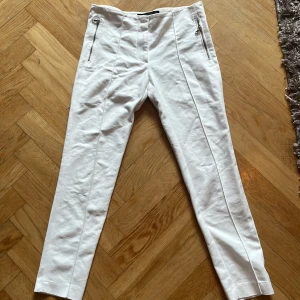 Vita kostymbyxor från Zara Basic - Snygga vita kostymbyxor från Zara Basic i storlek S. Byxorna har raka ben, hög midja och silverfärgade dragkedjor framtill som cool detalj. Materialet är mjukt och känns som bomull, perfekt för en clean och fräsch look.