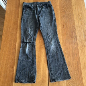 Svarta flare jeans från Old Navy size 16 (M) - Svarta jeans från Old Navy i flare-modell med hög midja. Jeansen har en snygg sliten look med en reva på ena benet och klassiska fem fickor. Tillverkade i jeansmaterial med en mörk tvätt och subtila slitningar.