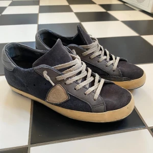 Phillipe model - Snygga mörkblå sneakers från Phillipe model med beige detaljer och logga på sidan. Skorna har ovandel i mocka och skinn, beige snörning och en kontrasterande beige sula. Perfekta för en avslappnad och stilren look.
