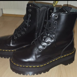 Svarta Dr. Martens Jadon kängor - Säljer ett par svarta Dr. Martens Jadon kängor i skinn med högt skaft, grov platåsula och den klassiska gula sömmen runt sulan. Kängorna har snörning framtill och dragkedja på insidan för enkel på- och avtagning. Perfekta för en cool stil.