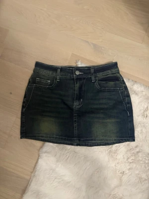 Mörk jeanskjol med detaljer på fickorna - Snygg mörkblå jeanskjol i kort modell med dekorativa detaljer. Kjolen är inte använd.