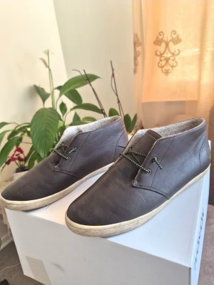 Fred Perry Skor, Brun läder med gröna detaljer, EUR 43 - Säljer ett par bruna loafers i läder med vita sulor och gröna snören med gröna detaljer. Skorna har en stilren design med låg profil och är perfekta för dig som gillar en avslappnad men ändå snygg look. Insidan är lätt fodrad för extra komfort.