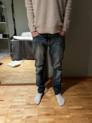 Blå jeans från Nudie Jeans - Säljer ett par klassiska blå jeans från Nudie Jeans med raka ben och snygga slitningar framtill. Jeansen har fem fickor och kontrastsömmar på bakfickorna. Tillverkade i denim med en avslappnad passform som passar perfekt till en casual stil.