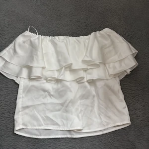 Vit offshoulder volangblus Gina Tricot - Superfin vit offshoulder blus från Gina Tricot med dubbla volanger upptill. Perfekt för dig som gillar en romantisk och trendig stil. Blusen är ärmlös och har en luftig passform med elastisk kant upptill. Endast använt 2 gånger