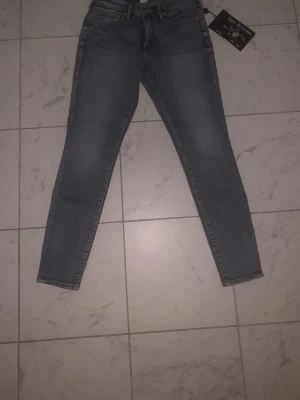 Blå slim fit jeans True Religion - Pris kan diskuteras!!! Säljer ett par kvinnojeans. Snygga blå slim fit jeans från True Religion med klassisk femficksdesign och gul broderad logga på ena bakfickan. Jeansen har normal midja och är tillverkade i denim med lätt tvättad look. Perfekta för en trendig och avslappnad stil.