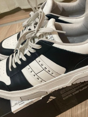 Tommy Jeans svartvita sneakers - Stilrena sneakers från Tommy Jeans i svart och vitt med tydlig logga på sidan. Skorna har snörning, rund tå och platt sula. Ovandelen är i syntetmaterial och designen är sportig men ändå klassisk.