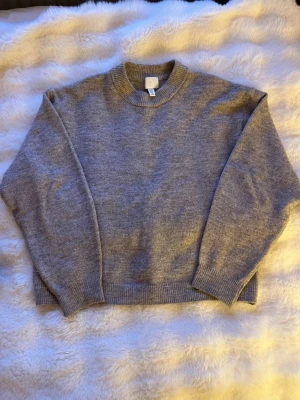 Grå stickad tröja från H&M - Mysig grå stickad tröja från H&M med rund halsringning och ribbade muddar vid ärmslut och nederkant. Varan är använt ett par gånger och är pyttelite nopprig, säljer billigt!