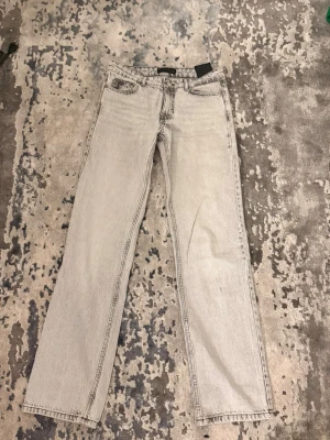 Ljusgrå raka jeans från Zara  - Säljer ett par ljusgrå jeans från Zara med rak passform och klassisk femficksdesign. Jeansen har hög midja och är tillverkade i ett robust denimtyg. Perfekta för en avslappnad och trendig look.