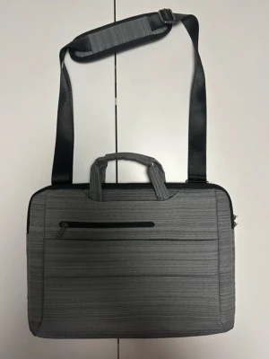 Goji laptopväska - Väskan har flera praktiska fack som gör det enkelt att organisera dina saker. På framsidan finns två separata fickor med dragkedja för snabb åtkomst till mindre tillbehör. På baksidan finns ett rymligt fack som passar bra för dokument eller andra platta föremål. Invändigt finns ett vadderat huvudfack anpassat för laptop samt extra utrymme för tillbehör.  Avtagbar och justerbar axelrem samt bekväma handtag upptill. Mycket fint skick, sparsamt använd. Passar perfekt för arbete, studier eller resor