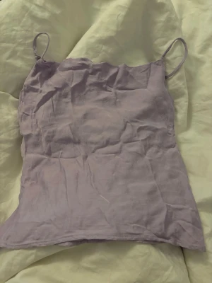 Ljuslila linnetopp från Kappahl - Säljer en ljuslila linnetopp från Kappahl med tunna axelband och mjuk, slät yta. Toppen har en enkel och stilren design som passar perfekt till sommaren. Materialet känns lätt och luftigt, och färgen är superfin till både jeans och kjol.