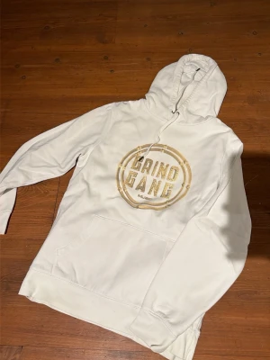 Grind Gang Music hoodies med tryck - Två hoodies från Grind Gang Music, en i vitt och en i svart, båda med stort guldigt tryck på bröstet. Klassisk huva med dragsko och magficka framtill. Perfekt för dig som gillar streetwear och vill sticka ut med snygg logga.