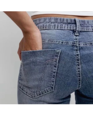 Blåa Lågmidjade bootcut jeans  - Säljer ett par helt oanvända blå bootcut jeans med låg midja och klassiska bakfickor. Jeansen har en snygg tvätt och kontrastsömmar som ger en retrovibe. Perfekta för dig som gillar en avslappnad men trendig stil.