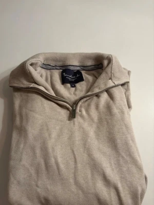 Beige halvziptröja  - Stilren beige stickad tröja från Bondelid med halvzip. Tröjan har en klassisk krage och är tillverkad i ett mjukt material som passar perfekt för lager-på-lager. Diskret broderad logga på bröstet, storlek S men passar M. Aldrig andvänd!