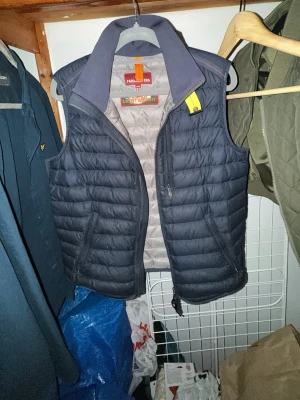 Mörkblå dunväst från Parajumpers - Snygg mörkblå dunväst från Parajumpers med quiltad design och hög krage. Västen har dragkedja framtill, två sidofickor och ljusgrå insida. Perfekt för lager-på-lager och ger en sportig look. Finns ett litet litet hål i ryggen. 