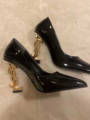 Svarta klackar från Saint Laurent - Säljer ett par svarta klackar från Saint Laurent med spetsig tå och klack i guld med YSL-loggan. De är helt oanvända och köpta av en på annan tjej. Varken box eller kvitto finns därav vet jag inte om de är äkta och därav det billiga priset. Storlek 37