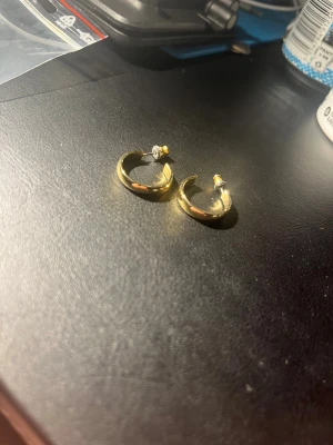 Guldiga hoops örhängen - Säljer ett par stilrena guldiga hoops örhängen i klassisk rund form. De är enkla och passar perfekt för dig som gillar minimalistiska smycken. Materialet ser ut att vara metall med guldfinish. Märke är okänt.