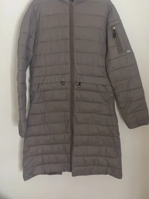 Lång dunjacka från CRW - Lång, dunjacka från CRW med dragkedja framtill, två fickor med lock och dragkedja på ärmen. Jackan har quiltad design och är perfekt för kalla vinterdagar i stallet. Tillverkad i lätt och värmande material.