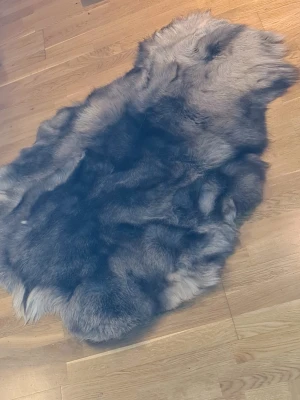 Grått renskinn i naturform - Säljer ett mjukt och fluffigt renskinn i grå och svarta nyanser. Skinnet har naturlig form och pälsen är tät och långhårig. Perfekt som inredningsdetalj på golv eller stol. Baksidan är ljus och slät.
