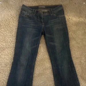 Blå bootcut jeans med låg midja - Snygga blå jeans med bootcut passform och låg midja. Jeansen har klassisk femficksdesign, slitningar framtill och är tillverkade i jeansmaterial. Perfekta för dig som gillar en avslappnad och trendig stil.