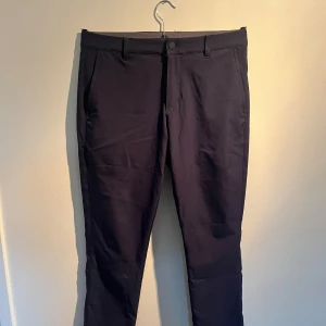 Mörkblå golfbyxor - Snygga mörkblå golfbyxor med slim passform och raka ben. Byxorna har klassiska fickor fram och bak, bälteshällor och stängs med knapp och dragkedja. Perfekta för en clean och stilren look. Materialet känns mjukt och har en lätt stretch.