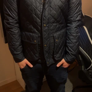 Ralph Lauren Jacka - Snygg mörkblå quiltad jacka från Polo Ralph Lauren med tryckknappar och två stora fickor framtill. Jackan har klassisk design och är perfekt för dig som vill ha en stilren look. Materialet är polyester och passformen är normal.