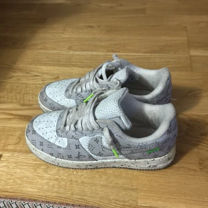 Gråvita nike air louisviton - Säljer ett par gråvita sneakers inspirerade av Nike Air Force 1 med monogrammönster och detaljer i neonlime på snörningen. Skorna har perforerad tå, platt sula och är tillverkade i skinnliknande material. Perfekt för dig som gillar unika och trendiga sneakers.