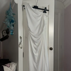 Vit långklänning med oneshoulder - Säljer en elegant vit långklänning med draperad design och oneshoulder-skärning. Klänningen har snygga rynkade detaljer vid axeln och en diskret dragkedja i sidan. Materialet är mjukt och följsamt, perfekt för dig som vill sticka ut med en stilren look. Hade den till min bal och endast använt 1 gång då jag inte vet när jag ska använda den igen ☺️ super fin och skit snygg, om du vill ha bilder med klänningen på kan jag fixa det 🥰‼️