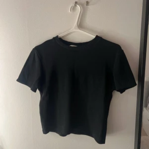 Svart stickad topp - En svart stickad topp med rund hals och korta ärmar. Enkel och stilren design som funkar till många olika looks. Ribbad kant vid halsen ger en snygg detalj. Perfekt för dig som gillar basic men ändå vill ha något som sticker ut lite.