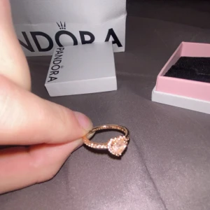 Pandora ring med rosa hjärta - Superfin ring från Pandora i roséguld med ett gnistrande hjärta i rosa sten och små rosa stenar längs hela ringen. Kommer i originalask och påse från Pandora. Ringen är knappt använd vilket då gör att jag känner att den är värd mycket eftersom att den är i original skick. Jag har för mig att ringen var i storlek 14 men den kan möjligtvis vara i storlek 16. Ringen är i 14 karat enligt hemsidan och original priset är 1000kr. Kom gärna med bud.