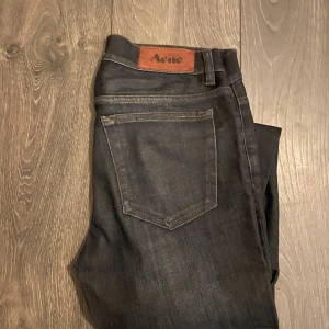 Svarta skinny jeans från Acne 30/34 - Snygga svarta jeans från Acne i modellen skinny med klassisk femficksdesign och diskret Acne-läderpatch bak. Jeansen är tillverkade i bomull med lite elastan för extra komfort och passform. Perfekta för dig som gillar stilrena och smala jeans.