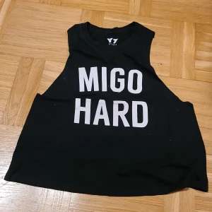 Svart linnetopp från Y7 Studio - Cool svart linnetopp från Y7 Studio med trycket 'MIGO HARD' i vitt på framsidan. Modellen är ärmlös och har breda axelpartier, perfekt för att visa upp armarna. Tillverkad i 100% bomull för en mjuk och skön känsla. Snygg och enkel att matcha med jeans eller shorts.