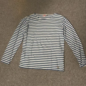 Randig långärmad tröja Armor Lux - Säljer en klassisk långärmad tröja från Armor Lux i storlek L. Tröjan är vit med marinblå horisontella ränder och har en rund halsringning. Tillverkad i mjuk bomull, perfekt för dig som gillar fransk stil och vill ha en chill look.