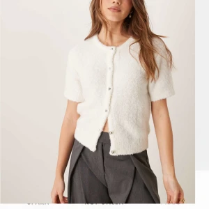 Vit kortärmad kofta från Gina Tricot - Supermysig vit kofta från Gina Tricot med korta ärmar och rund hals. Koftan är fluffig och stickad, har snygga silvriga knappar framtill och en lite loose passform. Perfekt för dig som gillar en chill och stilren look.🥰