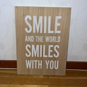 Smile and the World Smiles With You - En inspirerande träskylt med citatet 'Smile and the World Smiles With You'. Perfekt för att ge ditt rum en positiv vibe och påminna dig om att sprida glädje. Passar dig som vill ha peppande inredning och gillar motiverande budskap.