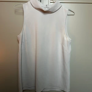 Vit polotopp från H&M, strl 36 - Säljer en stilren vit polotopp från H&M i storlek 36. Toppen är ärmlös med hög krage och har en rak, loose passform. Materialet känns mjukt och har en lätt glansig yta, troligen polyester. Dragkedja i nacken för enkel påklädning.🌟Använd ca 1-2 gånger 🤍