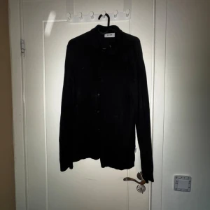 Svart skjorta från Only & Sons - Svart skjorta från Only & Sons med klassisk krage och knappar framtill. Skjortan har lång ärm och är tillverkad i ett mjukt material som känns skönt mot huden. Enkel och stilren design som funkar till många olika looks.