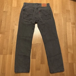 Levi's 551 grå jeans Straight Fit  - Säljer ett par Levi's 551 jeans i snygg mörkgrå tvätt. Klassisk femficksmodell med raka ben och normal passform. Jeansen har dragkedja, knappstängning och den ikoniska röda Levi's-taggen på bakfickan. Perfekt för dig som gillar tidlös streetstil.
