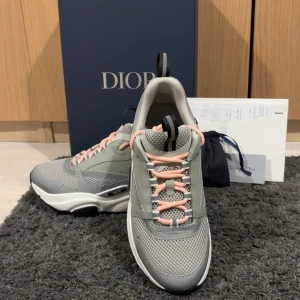 Grå bb22 sneakers  - Säljer ett par grå bb22 sneakers från  med mesh och skinnpaneler, vita och svarta detaljer på sulan samt ljusrosa snörning. Skorna har en rund tå, platt sula och reflekterande inslag på sidorna. Perfekt för dig som gillar exklusiv streetstyle. Kommer även med extra vita snören storlek 42 helt oanvända