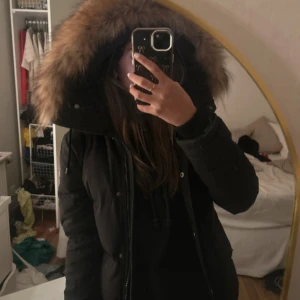 Hollies jacka - Säljer en svart pufferjacka med stor huva och fluffig päls runt kanten. Jackan har dragkedja och knappar framtill, samt långa ärmar och fickor med dragkedja. Perfekt för kalla dagar och riktigt snygg till jeans eller mjukis.