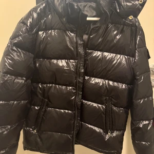 Moncler Svart pufferjacka med huva - Ny! Då den var fel storlek för mig. Använd knappt en vecka. Så nu blev den liggandes bara. Säljer en svart moncler pufferjacka med matt/glansig finish och huva. Jackan har två sidofickor med dragkedja och en kraftig dragkedja framtill. Perfekt för kalla dagar och har en riktigt schysst streetstil. Passar dig som gillar en lite oversized look.
