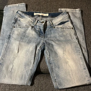Lågmidjade jeans - Säljer ett par ljusblå jeans från 72D med snygga slitningar och tvättad look. Jeansen har kontrastsömmar och raka ben. Materialet är jeans och har detaljerade bakfickor med broderi. Midjan är W26 och passar på mig som är 170