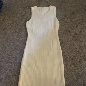 Vit ribbad ärmlös klänning S - Säljer en vit, ribbstickad ärmlös klänning i storlek S. Klänningen har v-ringning och är figurnära med en mjuk, stretchig känsla. Materialet är 100% akryl och den är perfekt för dig som gillar en enkel men stilren look. Perfekt som vinter klänning .