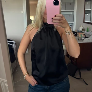 Svart halterneck linnetopp i satin - Säljer en svart halterneck linnetopp i glansigt satinmaterial. Helt nytt skick!! 