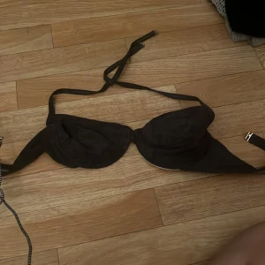 Svart bikiniöverdel med knyt - Snygg svart bikiniöverdel med bygel och vadderade kupor. Knytband i nacken och klassisk stängning i ryggen. Utsidan är svart och insidan vit, vilket ger en clean kontrast. Perfekt för stranden eller poolen.