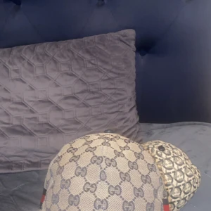 Gucci keps GG canvas beige - Säljer en ikonisk Gucci keps i beige canvas med klassiskt GG-monogram över hela kepsen och röd-blå rand på sidan. Justerbar rem baktill i läder. Perfekt accessoar för dig som vill sticka ut med lyxig streetstyle.