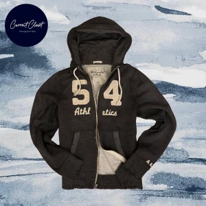 Mörkgrå hoodie från Abercrombie & Fitch - Mörkgrå hoodie med dragkedja från Abercrombie & Fitch | Stor broderad 54 och texten Athletics framtill, vita snören i huvan och fickor på magen | Size M, passar M | Smådefekter kommer men ska vara så för vintage stil