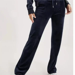 Mörkblå mjukisbyxor med snörning - Snygga mörkblå mjukisbyxor i mjukt velourmaterial med raka ben och hög midja. Byxorna har snörning i midjan, fickor fram och bak med knappdetaljer. Perfekta för chill dagar och en avslappnad stil.